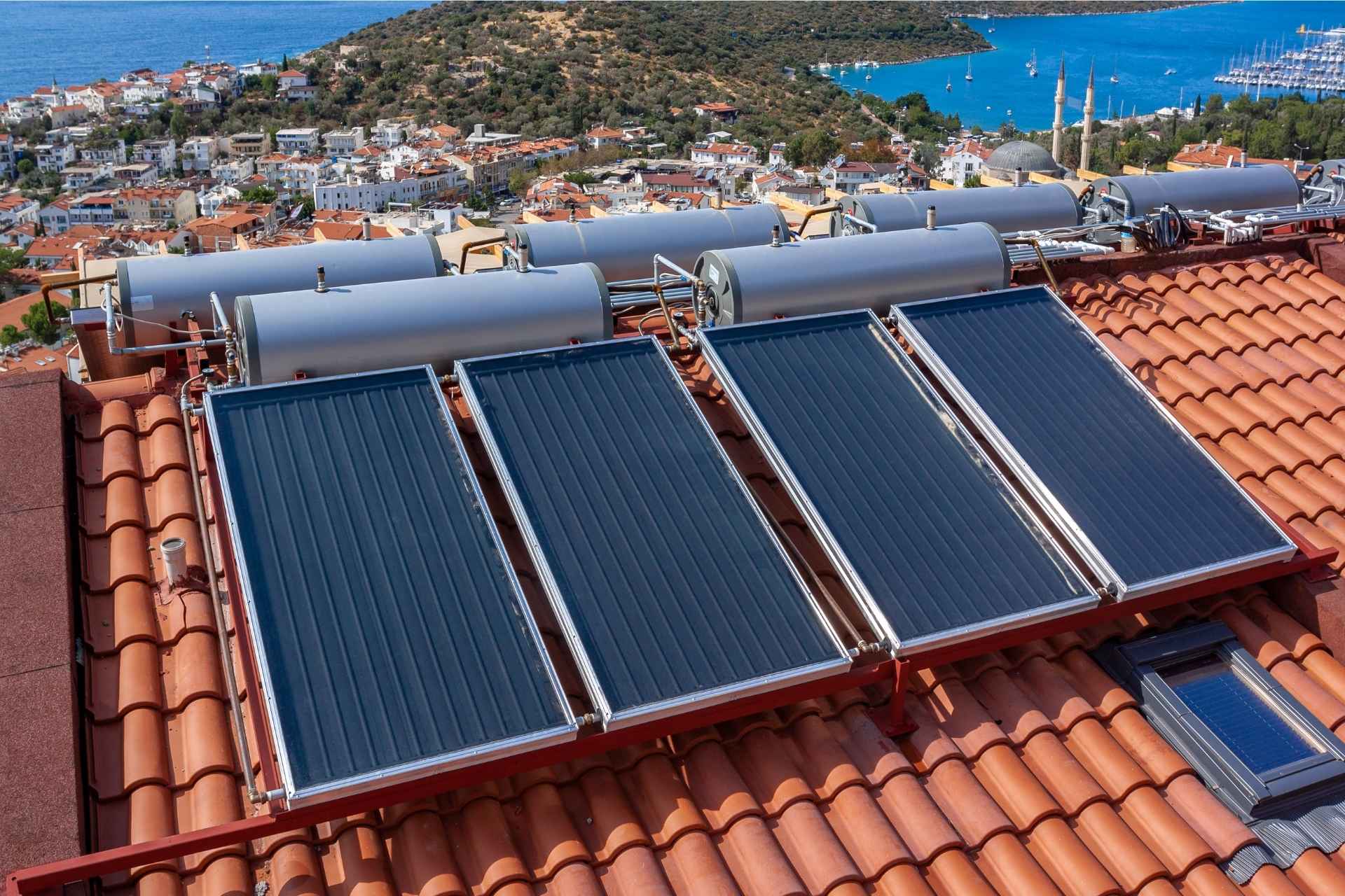 Image montrant des ballons d'eau chaude solaire Ulticom, installés sur le toit d'un bâtiment dans une ville côtière. Les panneaux de couleur bleu foncé sont alignés sur le toit. L'image illustre l'utilisation de l'énergie solaire thermique pour chauffer l'eau.