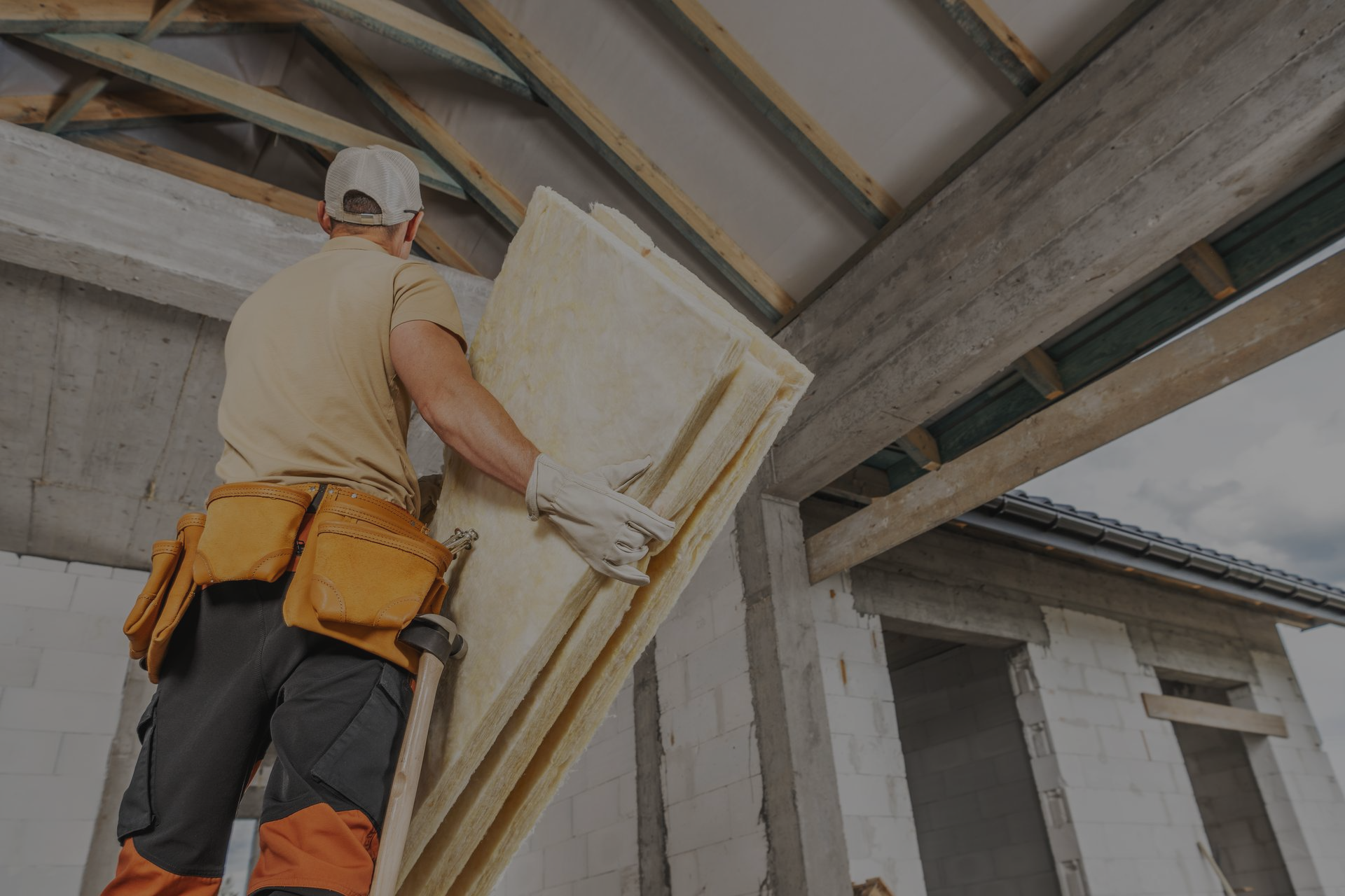 Artisan, équipé d'outils, posant des panneaux d'isolation Ulticom en laine minérale sous un toit en construction