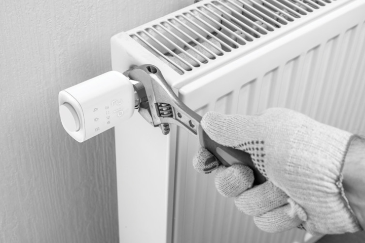 Technicien ajustant un thermostat connecté sur un radiateur avec une clé à molette